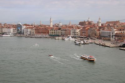 Boats in river by buildings in city against sky