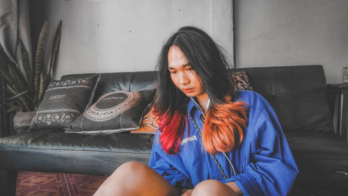 Young woman looking down while sitting on sofa at home