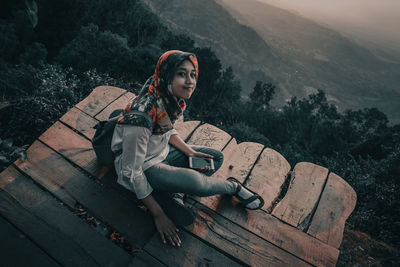 Portrait of woman sitting on bench at mountain