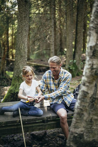 Smiling father helping daughter in cutting on footbridge in forest