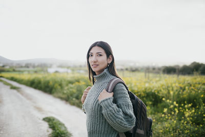 Portrait of woman with backpack standing near field against clear sky
