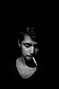 Portrait of young woman smoking over black background