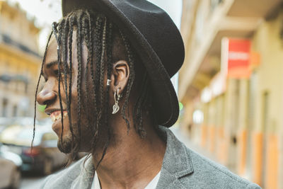 Close-up of smiling young man with braided hair wearing hat in city