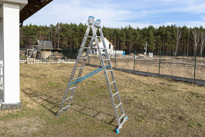 A tall, fold-out aluminum ladder standing in the yard, in the shape of a triangle.