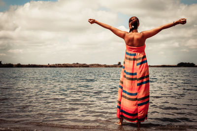 Rear view of woman standing at beach against sky