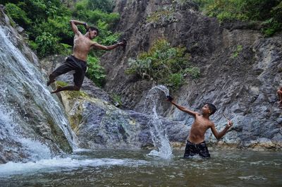 Full length of shirtless man standing on rock against waterfall