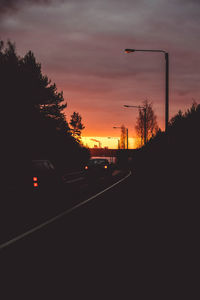 Cars on street against sky at sunset