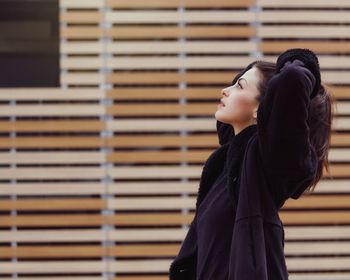 Side view of thoughtful young woman with hand in hair by building