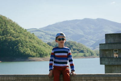 Boy sitting on railing against river