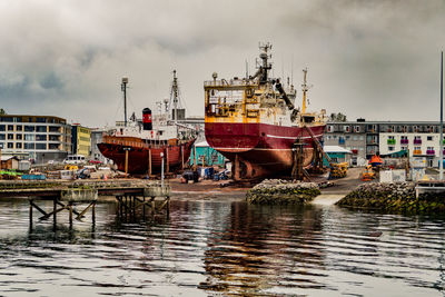 Fishing boats moored at harbor against sky