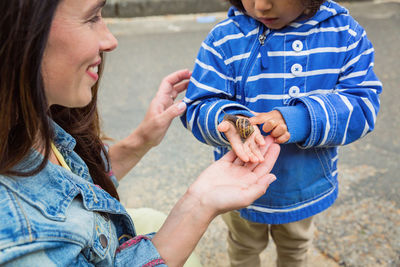 Mother and little handsome baby boy playing outdoor with snail