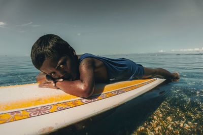 Portrait of boy lying on surfboard over sea