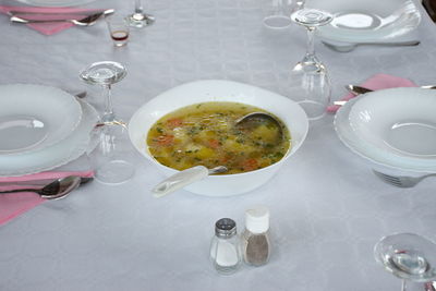 Table with white tablecloth preparing for dinner - soup in a white bowl