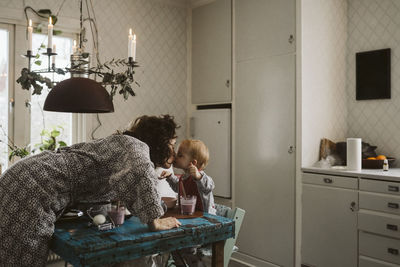 Affectionate mother kissing daughter sitting at dining table in kitchen