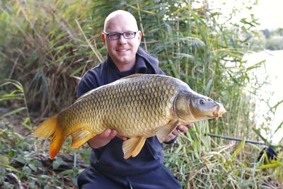 Portrait of man holding fish standing against plants 