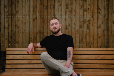 Portrait of man sitting on wooden wall