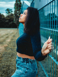 Side view of young woman standing against fence