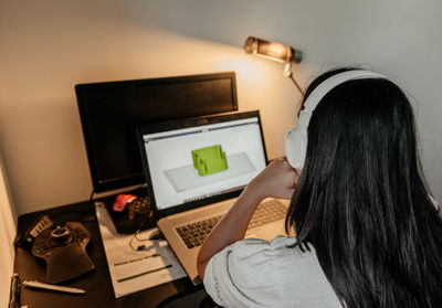 Rear view of young businesswoman sitting at desk, using laptop and 3d design software