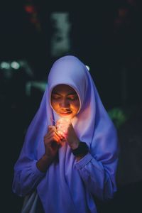 Woman wearing headscarf holding string light at night