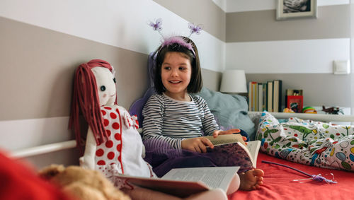 Smiling girl wearing fairy costume while sitting with book on bed at home