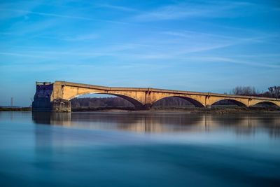 Arch bridge over river against blue sky