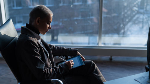 Man using mobile phone while sitting on window