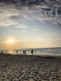 People on beach against sky during sunset