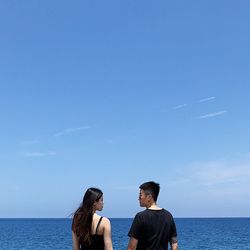 Rear view of couple standing in sea against blue sky