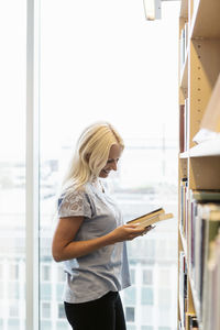 Side view of young woman reading book in university library