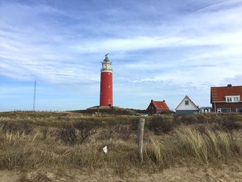 Lighthouse on field by building against sky