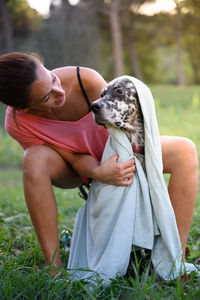 Side view pretty woman drying her dog with a towel after a bath in the garden. pet care concept.