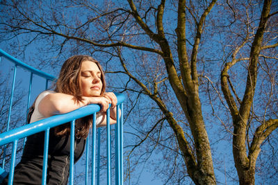 Low angle view of woman looking at bare tree against blue sky