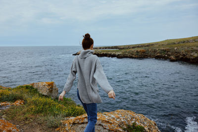 Rear view of woman standing on rock by sea against sky