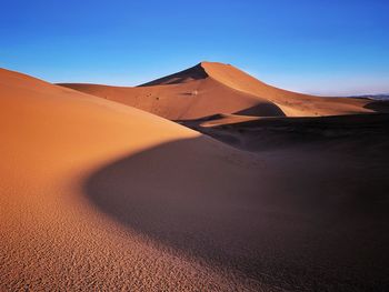 Sand dunes in desert against clear blue sky