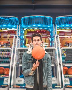 Portrait of young man spinning basketball against amusement arcades