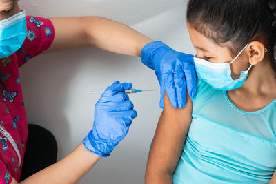 Children's nurse injecting arm of little brown girl, girl watching injection. 