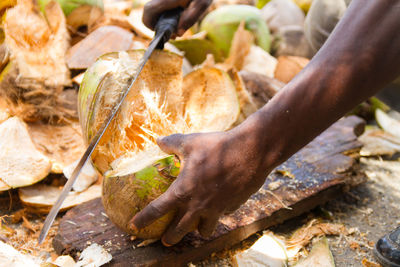 Cropped man cutting coconut with machete on board