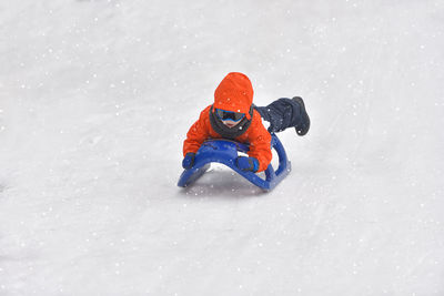 Full length of boy tobogganing on snowy field