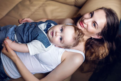 Young happy mother in white tank top laying with my son on a light sofa in the apartment