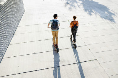 Back view of couple with backpacks riding electric scooters