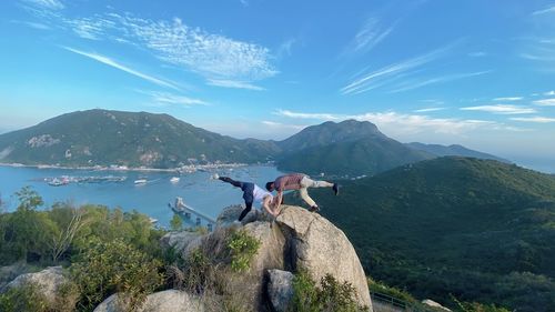 People on rock by mountains against sky