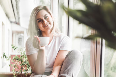 Portrait of young woman holding coffee cup sitting at home