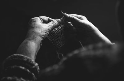 Midsection of person knitting crochet in darkroom