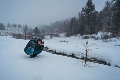 Man photographing crouching on snow covered land