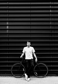 Portrait of young man standing by bicycle against wall