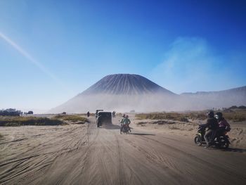 People riding motorcycles on desert against blue sky