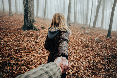 Cropped hand of man holding woman at forest during autumn