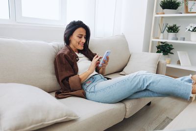 Young woman using phone while sitting on sofa at home
