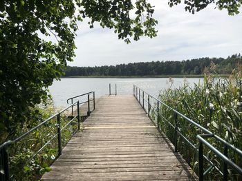 Empty wooden pier over lake against sky