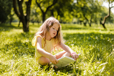 A little girl is sitting with a book in the garden. a girl reads a book on a summer day